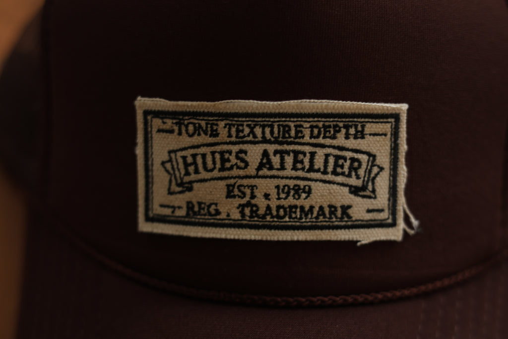 Close-up of Hues Atelier embroidered patch on trucker hat