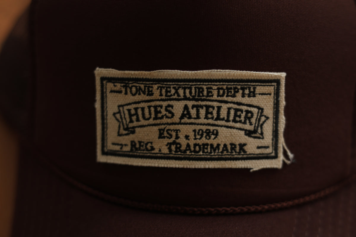 Close-up of Hues Atelier embroidered patch on trucker hat