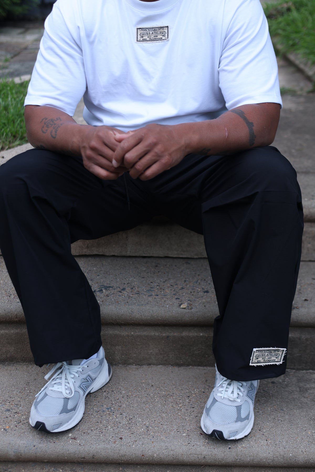 Seated model wearing the Hues Atelier Ivory Tee with black pants